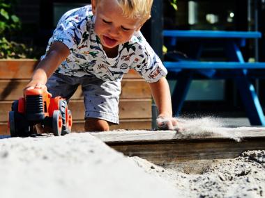 Billede af et barn, som leger i en sandkasse med en traktor