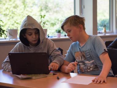 2 drenge som sidder og arbejder foran en bærbar computer